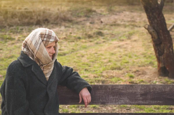 Eine ernste Seniorin sitzt auf einer Bank und schaut weg. Porträt einer nachdenklichen alten Großmutter, die sich an den Stock lehnt — Stockfoto