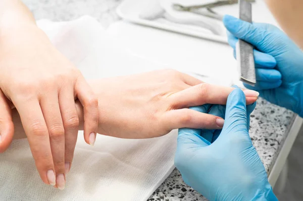 Nail technician giving a customer a manicure at nail salon. Young caucasian woman receiving a manicure