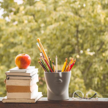 Okula geri dön ve mutlu zaman! Elma, pencerede kitap ve kalem yığını