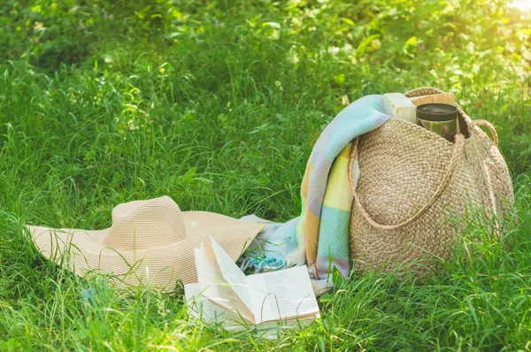 Straw bag, book, hat and thermo cup on a sunny summer day