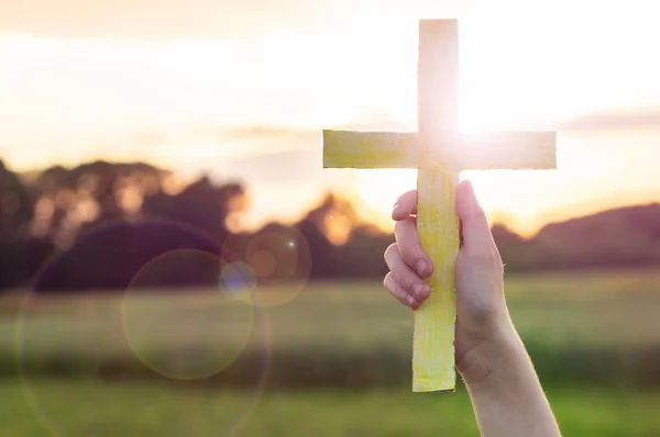 Gadis remaja memegang salib di tangan selama matahari terbenam yang indah. Tangan dilipat dalam konsep doa untuk iman — Stok Foto
