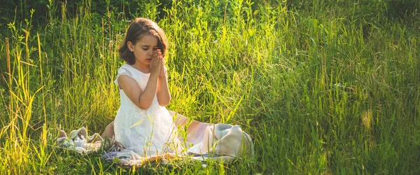 Niña cerró los ojos, rezando en un campo durante el hermoso atardecer. Manos dobladas en concepto de oración por la fe —  Fotos de Stock