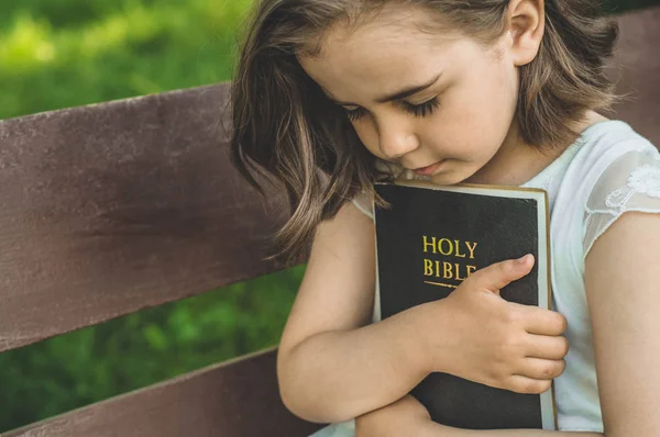 Membaca Alkitab di luar ruangan. Kristen gadis memegang Alkitab di tangannya duduk di bangku — Stok Foto