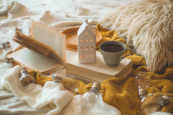 Still life details in home interior of living room. Sweaters and cup of tea with a candle house and autumn decor on the books — Stock Photo, Image