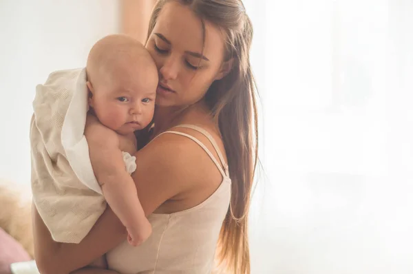 Otthon portréja egy újszülött az anya az ágyon. Anya gazdaság és megcsókolta a gyerekét. — Stock Fotó