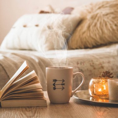 Kitap, kahve fincanı ve ev arka planda birçok mum. Ev ve ev dekorasyonu. Mumlar alev