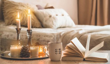 Kitap, kahve fincanı ve ev arka planda birçok mum. Ev ve ev dekorasyonu. Mumlar alev