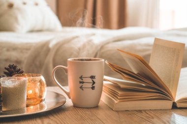 Kitap, kahve fincanı ve ev arka planda birçok mum. Ev ve ev dekorasyonu. Mumlar alev