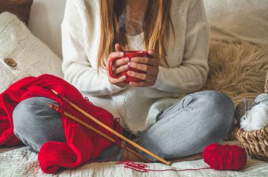 Güzel kız yatakta sıcak bir fincan çay ile sıcak bir kazak örer. Hobi olarak örgü