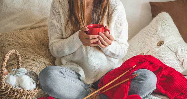 Krásná dívka si odkrájí Teplý svetr s horkou šálkem čaje na posteli. Pletení jako hobby — Stock fotografie