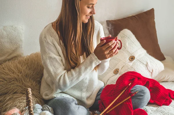 Hermosa chica teje un suéter caliente con una taza de té caliente en la cama. Tejer como hobby — Foto de Stock