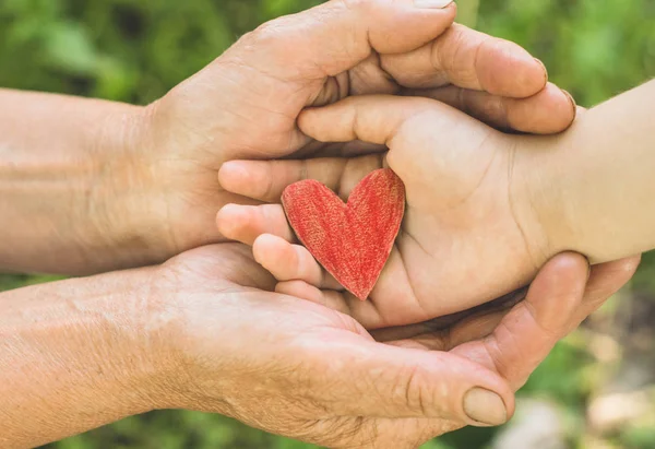 Childs mano y abuela mano vieja sostienen el corazón. Concepto idea de amor familia proteger a los niños y ancianos abuela — Foto de Stock