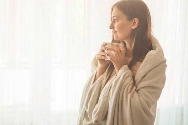 Mujer con una taza de bebida caliente junto a la ventana. Mirando la ventana y bebiendo té. Buenos días con el té. — Foto de Stock