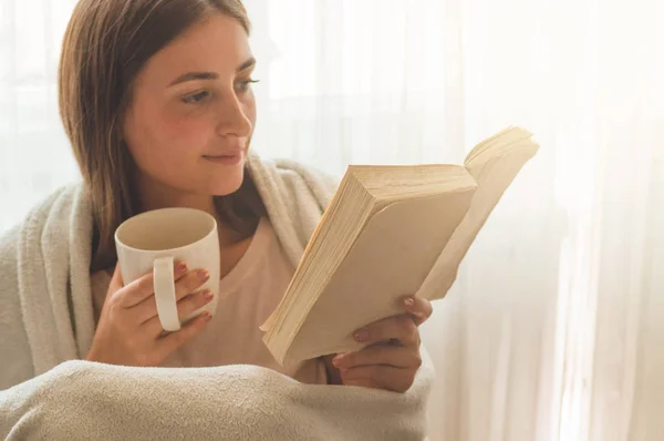 Krásná dívka si čte knihu s šálkem horkého čaje. Podzim zimní čas. — Stock fotografie