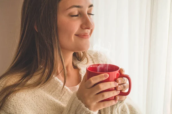 Femme avec une tasse de boisson chaude près de la fenêtre. Je regarde la fenêtre et je bois du thé. Bonjour avec le thé — Photo