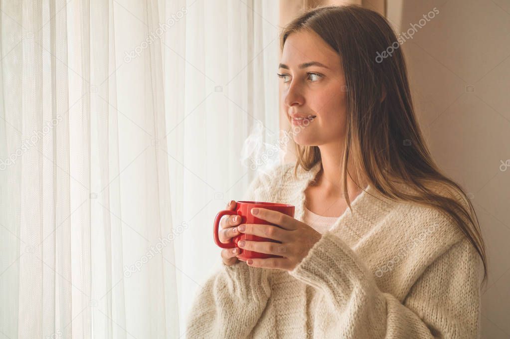 Woman with cup of hot drink by the window. Looking at window and drink tea. Good morning with tea