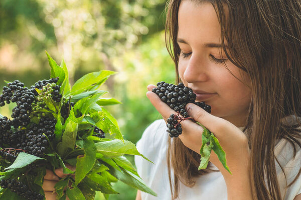 Девушка держит в руках кластеры фруктов черной бузины в саду (Sambucus nigra). Старейшина, черная бузина
.