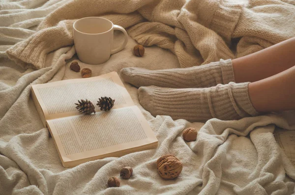 Gemütlicher Herbstwinterabend, warme Wollsocken. Frau liegt auf weißer zotteliger Decke und liest Buch — Stockfoto