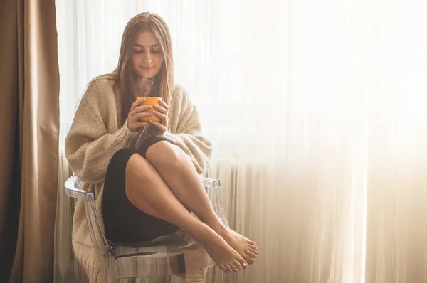 Mujer con una taza de bebida caliente junto a la ventana. Mirando la ventana y bebiendo té. Buenos días con el té. . — Foto de Stock