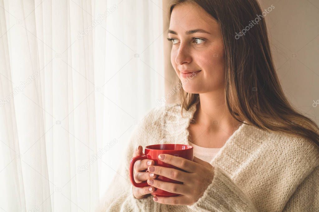 Woman with cup of hot drink by the window. Looking at window and drink tea. Good morning with tea. 