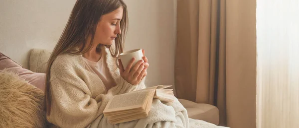 Útulný zimní podzimní večer. Žena pije horký čaj a čtení knihy. — Stock fotografie