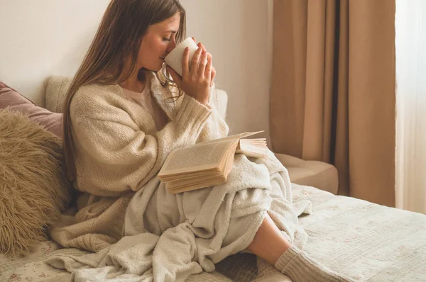 Acogedora noche de invierno de otoño. Mujer bebiendo té caliente y leyendo libro . — Foto de Stock