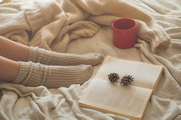 Acolhedor Outono noite de inverno, meias de lã quente. Mulher está deitado pés para cima no cobertor desgrenhado branco e livro de leitura — Fotografia de Stock