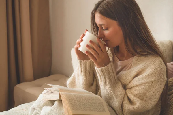 Acogedora noche de invierno de otoño. Mujer bebiendo té caliente y leyendo libro . — Foto de Stock