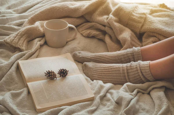 Cozy Autumn winter evening , warm woolen socks. Woman is lying feet up on white shaggy blanket and reading book