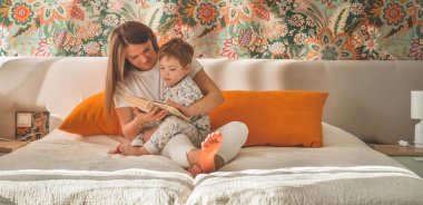 Güzel genç anne, modern iç mekanda küçük oğluna kitap okuyor.