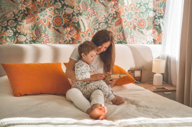 Güzel genç anne, modern iç mekanda küçük oğluna kitap okuyor.