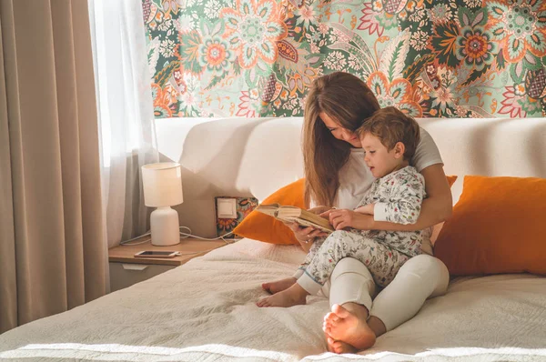 Güzel genç anne, modern iç mekanda küçük oğluna kitap okuyor.