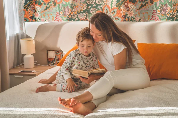 Csinos fiatal anya könyvet olvas a kisfiának a modern belső térben. — Stock Fotó