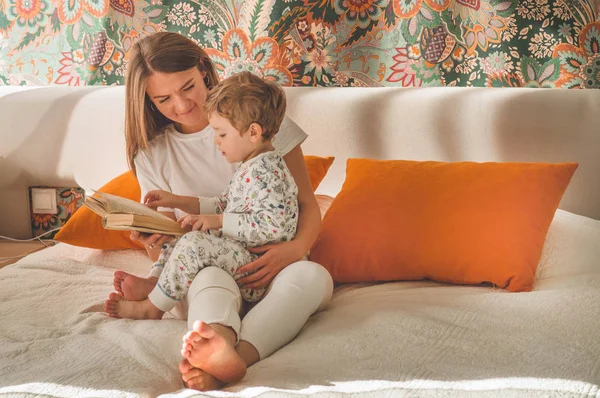 Linda madre joven leyendo un libro a su pequeño hijo en el interior moderno —  Fotos de Stock