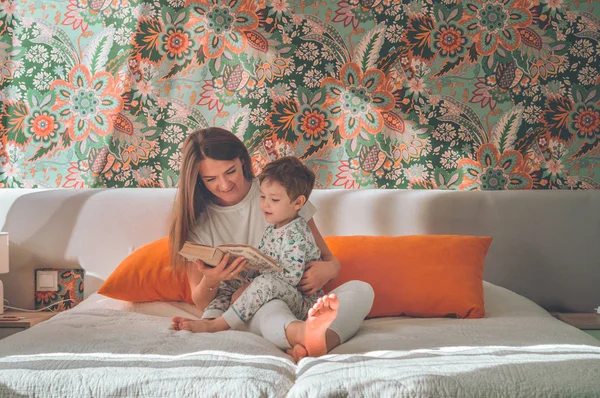Linda madre joven leyendo un libro a su pequeño hijo en el interior moderno —  Fotos de Stock