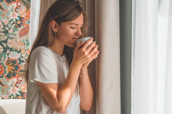 Žena s šálkem horkého nápoje u okna. Dívám se na okno a piju čaj. Dobré ráno s čajem. — Stock fotografie