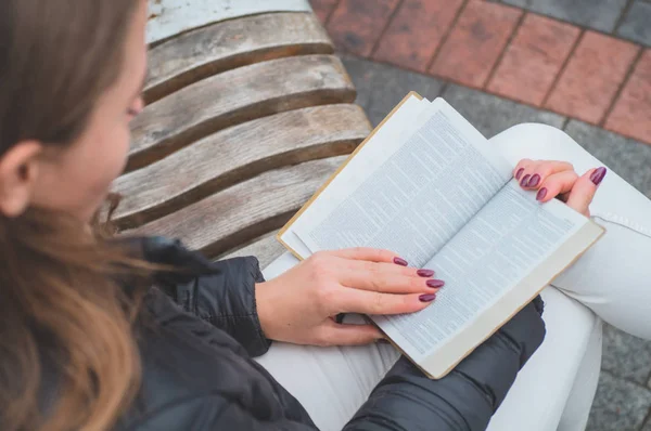 Girl holds book in her hands. The girl sitting on a bench, reading a book. — Stock Photo, Image