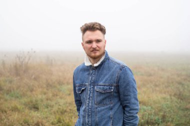 Bıyıklı, düşünceli, genç, stil sahibi bir adam gri sisli arka plana karşı duruyor..