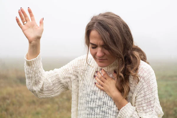 Девушка закрыла глаза, молясь в поле во время прекрасного тумана. Руки сложены в молитвенной концепции веры — стоковое фото