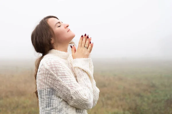 Chica cerró los ojos, rezando en un campo durante la hermosa niebla. Manos dobladas en concepto de oración por la fe —  Fotos de Stock