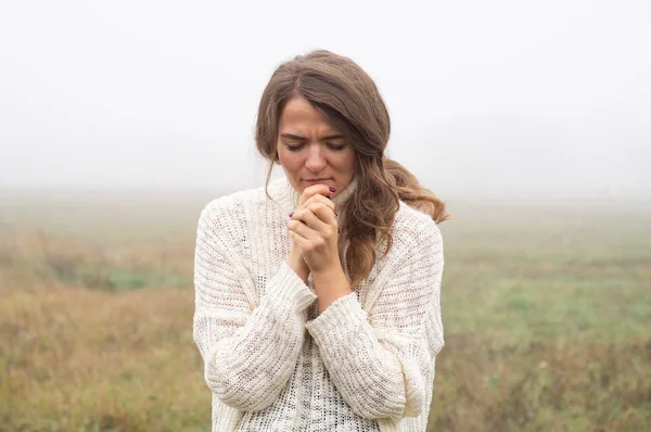 Ragazza chiuse gli occhi, pregando in un campo durante la bella nebbia. Mani giunte nel concetto di preghiera per la fede Fotografia Stock