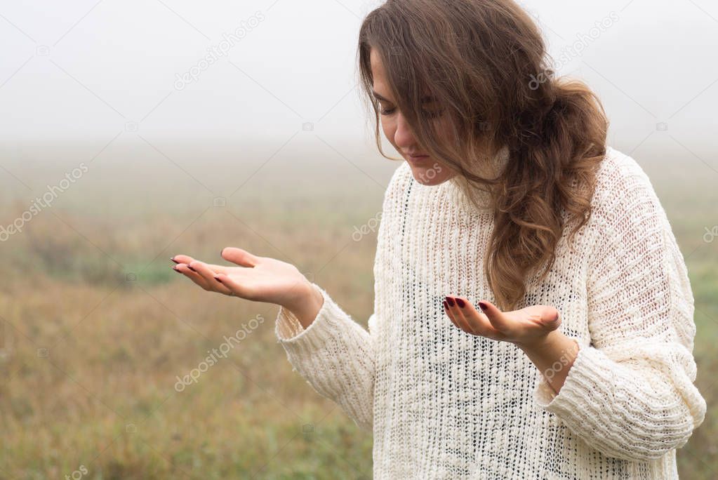 Girl closed her eyes, praying in a field during beautiful fog. Hands folded in prayer concept for faith