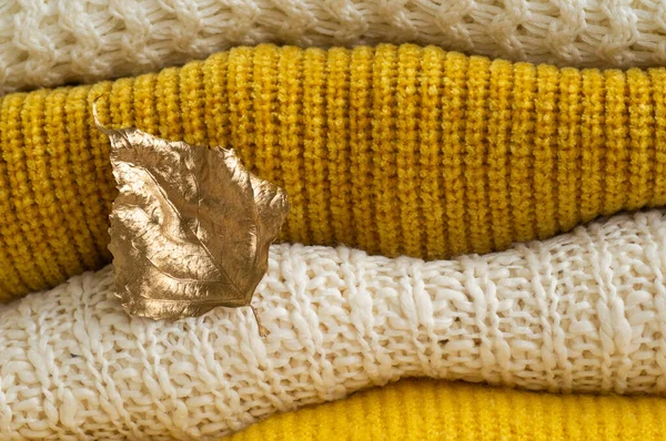 Autumn winter concept. Pile of knitted clothes with autumn gold leaves, warm background, knitwear — Stock Photo, Image