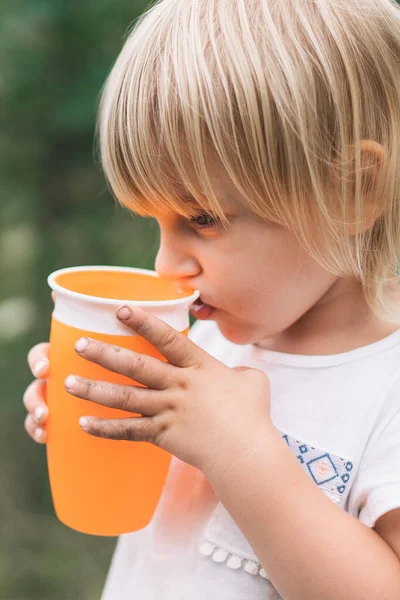 Gadis kecil yang cantik dengan tangan kotor minum dari cangkir — Stok Foto