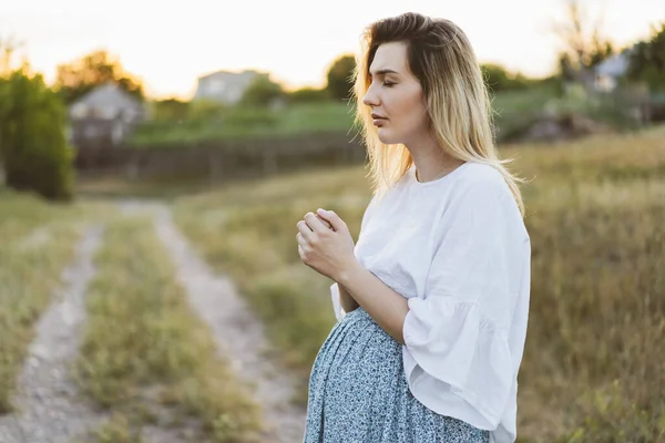 Pregnant woman praying outdoors on at sunset. Concept for faith, spirituality and religion. — Stock Photo, Image