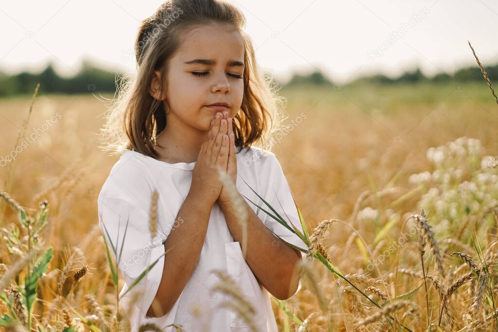 Little Girl closed her eyes, praying in a field wheat. Hands folded in prayer. 
