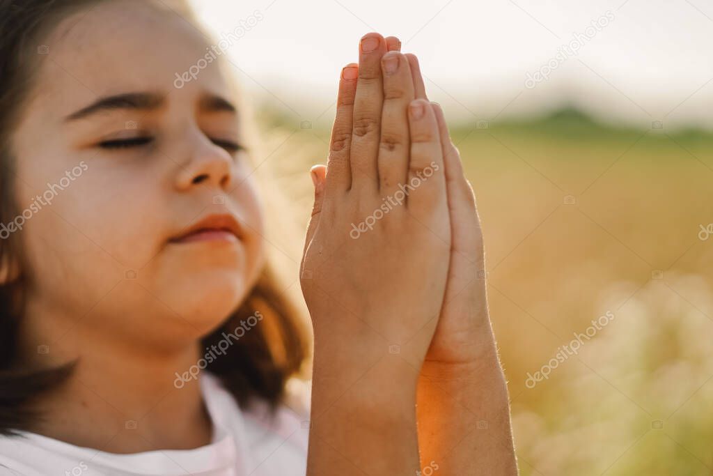 Little Girl closed her eyes, praying in a field wheat. Hands folded in prayer. 