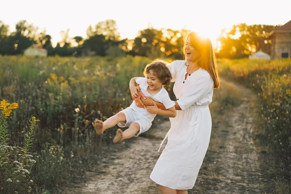 Frau spielt bei Sonnenuntergang mit ihrem Kind auf dem Feld — Stockfoto