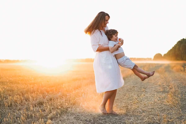 Frau spielt bei Sonnenuntergang mit ihrem Kind auf dem Feld — Stockfoto
