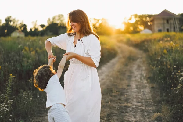 Mulher brincando com seu filho no campo durante o pôr do sol — Fotografia de Stock